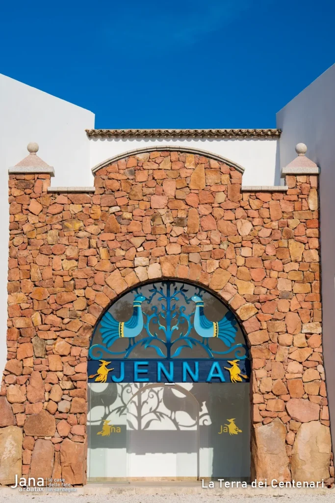 Dettaglio dell'arco in pietra del portale di Borgo Jenna, con la vetrata, la scritta Jenna e due pavoncelle sarde attorno all'albero della vita.